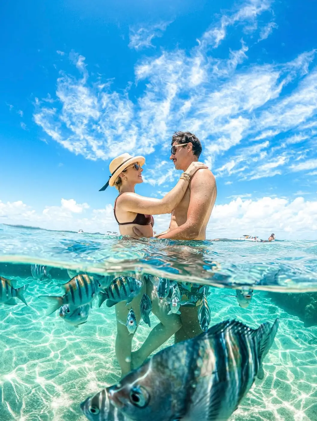 Casal fotografado meio dentro, meio fora da água com peixes