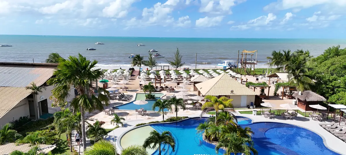 Vista aérea do Pontal do Maragogi: piscina entre palmeiras, guarda-sóis na areia e o mar